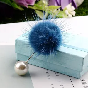 Detailansicht einer blauen Nerzpelz-Brosche mit weißer Perle auf einer blauen Geschenkbox.