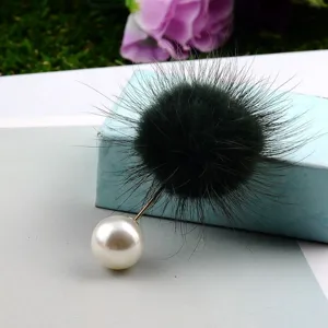Detailaufnahme einer Brosche aus Nerzpelz-Pompon und großer weißer Perle mit goldener Nadel