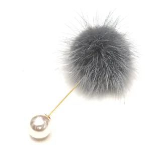 Detailansicht einer hochwertigen grauen Nerzfell-Bommel und eleganten weißen Perlenbrosche