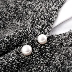 Makroansicht von eleganten weißen Perlen-Broschen auf einem strukturierten grauen Strick-Cardigan.