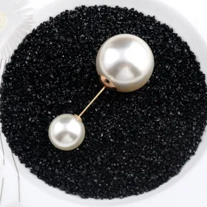 Detail einer eleganten Brosche mit zwei Perlen auf dekorativem schwarzem Sand