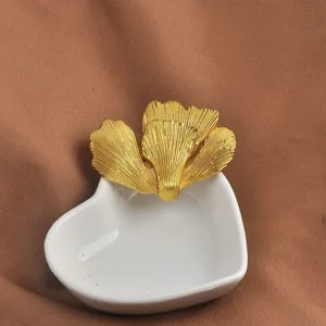 Primo piano di una spilla vintage a foglia di ginkgo in metallo dorato su vassoio cuore.