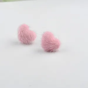 Nahaufnahme der rosafarbenen, flauschigen Herzohrringe aus Nerzfell für den Winter