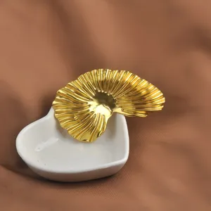 Primo piano di una spilla a foglia di ginkgo dorata su un piatto a cuore bianco