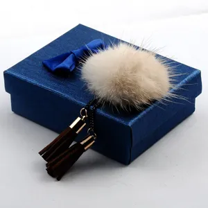 Detailansicht einer flauschigen Nerzfell-Brosche mit braunen Wildleder-Quasten auf blauer Box