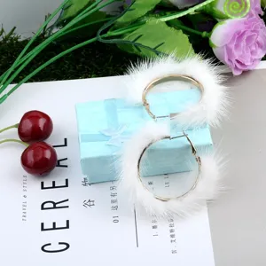 Detalle de pendientes de aro de piel de visón blanco sobre una caja de regalo azul.