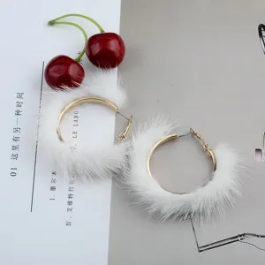 Primer plano de pendientes de aro dorados decorados con suave pelo de visón blanco.