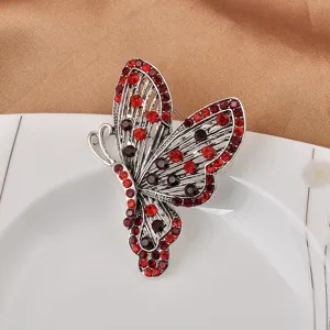 Detaillierte Makroansicht einer silbernen Schmetterlingsbrosche mit roten Steinen.