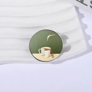 Künstlerische runde Brosche mit Illustration einer Person, die in eine Kaffeetasse taucht.