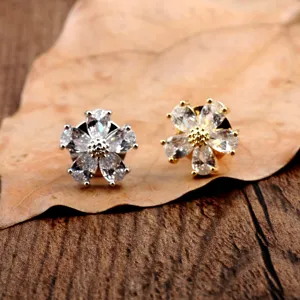 Detailansicht von silbernen und goldenen Zirkon-Blumenbroschen auf rustikalem Blatt