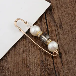 Nahaufnahme einer eleganten goldenen Sicherheitsnadel-Brosche mit weißen Perlen.