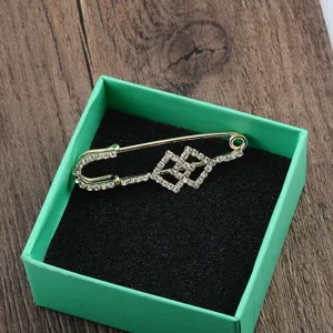 Detailansicht einer goldfarbenen Brosche mit geometrischen Strasssteinen in grüner Box.