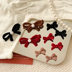 Elegant velvet bow hair clips with pearl detail on a decorative mirror backdrop.