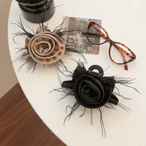 Elegant rose hair clips with feathers in black and beige colors displayed with glasses