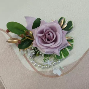 Detail close-up shot of purple artificial rose wedding corsage with pearls and gold leaves.