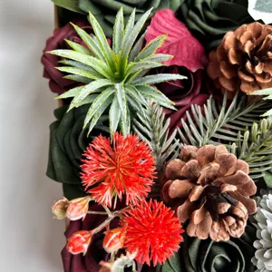 Vue détaillée fleurs artificielles Noël boîte cadeau DIY avec roses, pommes de pin et verdure.