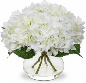 Gros plan d'hortensias blancs artificiels dans un vase en verre avec de l'eau transparente.