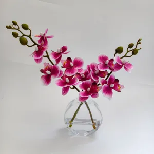 Vue détaillée d'un arrangement d'orchidées artificielles dans un vase en verre avec de l'eau fausse.