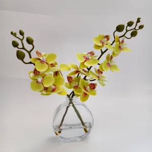 Vue détaillée d'orchidées jaunes artificielles en vase en verre transparent avec de l'eau.