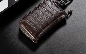 Detail van bruine krokodillenleer autosleuteletui, fijne textuur, rits en metalen haak.