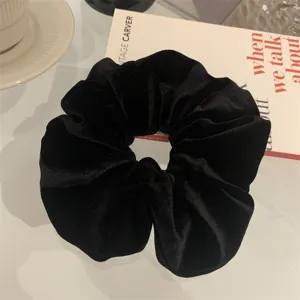 Detailed view of a premium black velvet scrunchie hair tie on a minimalist white table