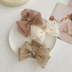 Détail de chouchous à nœud en organza avec strass en crème et beige sur assiette blanche