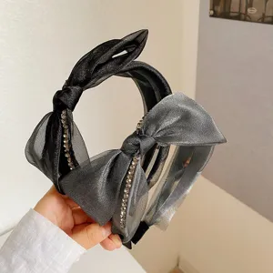 Primer plano de una elegante diadema con lazo de malla negra y detalles de pedrería.