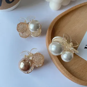 Detail shot of elegant mini pearl hair claw clips with cherry design on a wooden tray
