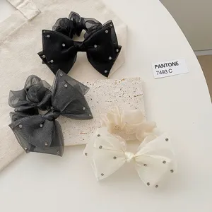 Détail de trois chouchous nœuds en organza et strass noirs, gris et crème.