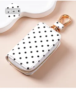 Weißes Leder-Autoschlüssel-Etui mit schwarzen Punkten, goldenem Reißverschluss und Haken.
