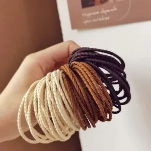 Detailed macro view of braided milk tea colored elastic hair ties held in hand for hair styling.
