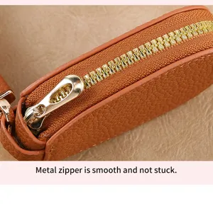 Detailed close-up view of brown textured leather key case featuring smooth gold metal zipper.