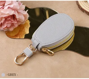 Grey leather car key case detail showing gold zipper and metal clasp on a reflective tray.
