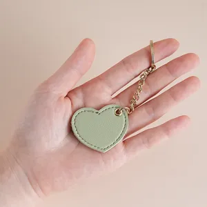 Cute heart-shaped green leather keychain held in hand, stylish bag charm and car key ring.