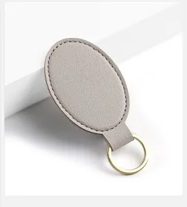 Llavero ovalado de cuero PU gris vista detallada con anillo dorado y costuras finas.