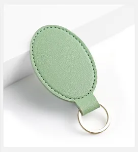 Detalle de primer plano del llavero de cuero PU ovalado verde menta con costuras y anilla dorada.