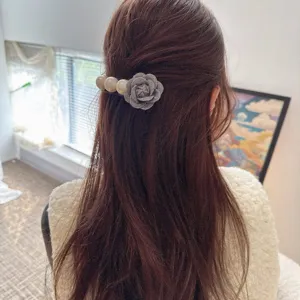 Detailed view of an elegant grey fabric flower and pearl hair comb styled on wavy brown hair