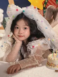 Detailed view of a girl's white birthday veil featuring colorful pom-poms and lace
