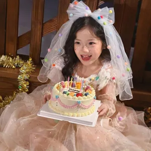Children's white birthday veil featuring colorful pom-poms and a large mesh bow