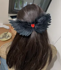 Close-up of black feather wing hair clip with red heart gem for Halloween cosplay