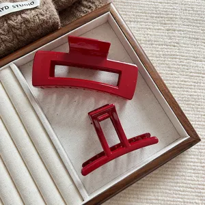 Detalle de pinzas rectangulares para el pelo en rojo brillante sobre una bandeja texturizada crema.