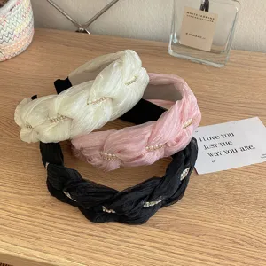 Detailopname van drie gevlochten haarbanden in wit, roze en zwart met parels