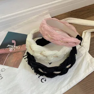 Detailweergave van drie Franse gevlochten haarbanden in roze, crème en zwart met parels.