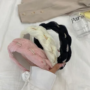 Detailweergave van drie Franse gevlochten haarbanden in de kleuren roze, crème en zwart