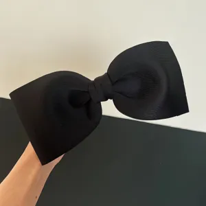 Detailed view of an oversized black bow hair clip showing its elegant fabric texture