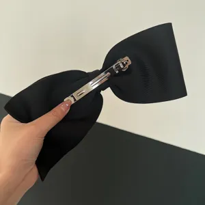 Detail of large black grosgrain bow hair clip with silver spring steel fastener.