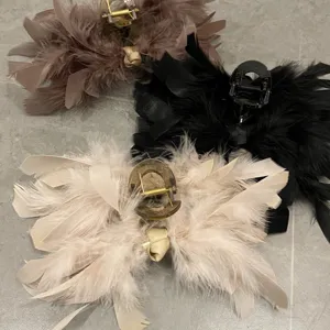 Detailed view of three large ostrich feather hair claw clips in brown, black, and beige
