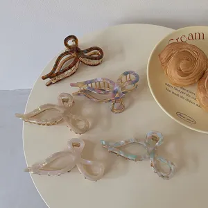 Elegant acetate bow hair claw clips in marble patterns displayed on a cafe table scene