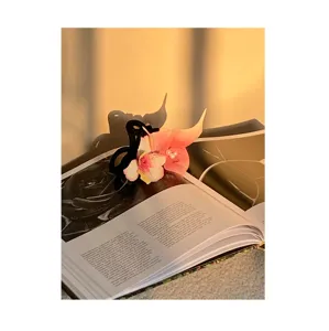Detailed view of a pink orchid flower hair clip with pearls resting on a book