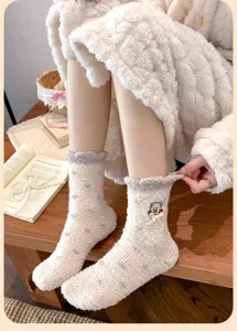 Nahaufnahme von süßen cremefarbenen Korallenvlies-Socken mit Bärenstickerei und Schleife.